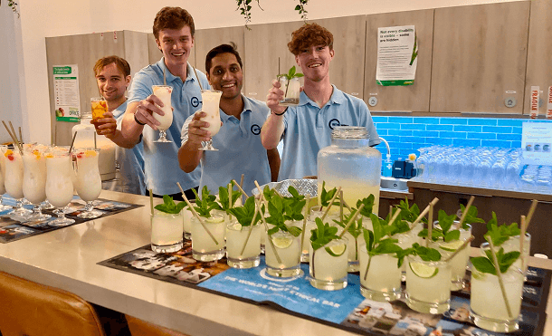 Four professional team members smiling and raising sustainable cocktails behind a mobile pop up bar representing our evolution into a premium ethical event bar service