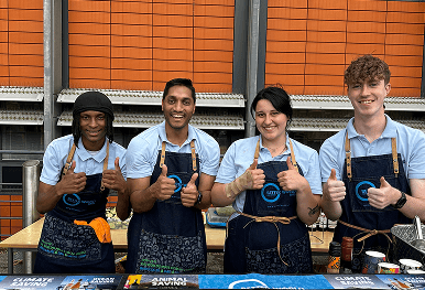 Four professional team members smiling and giving a thumbs up behind an ethical pop up bar representing our mission to transform lives by providing vital hospitality employment for vulnerable individuals