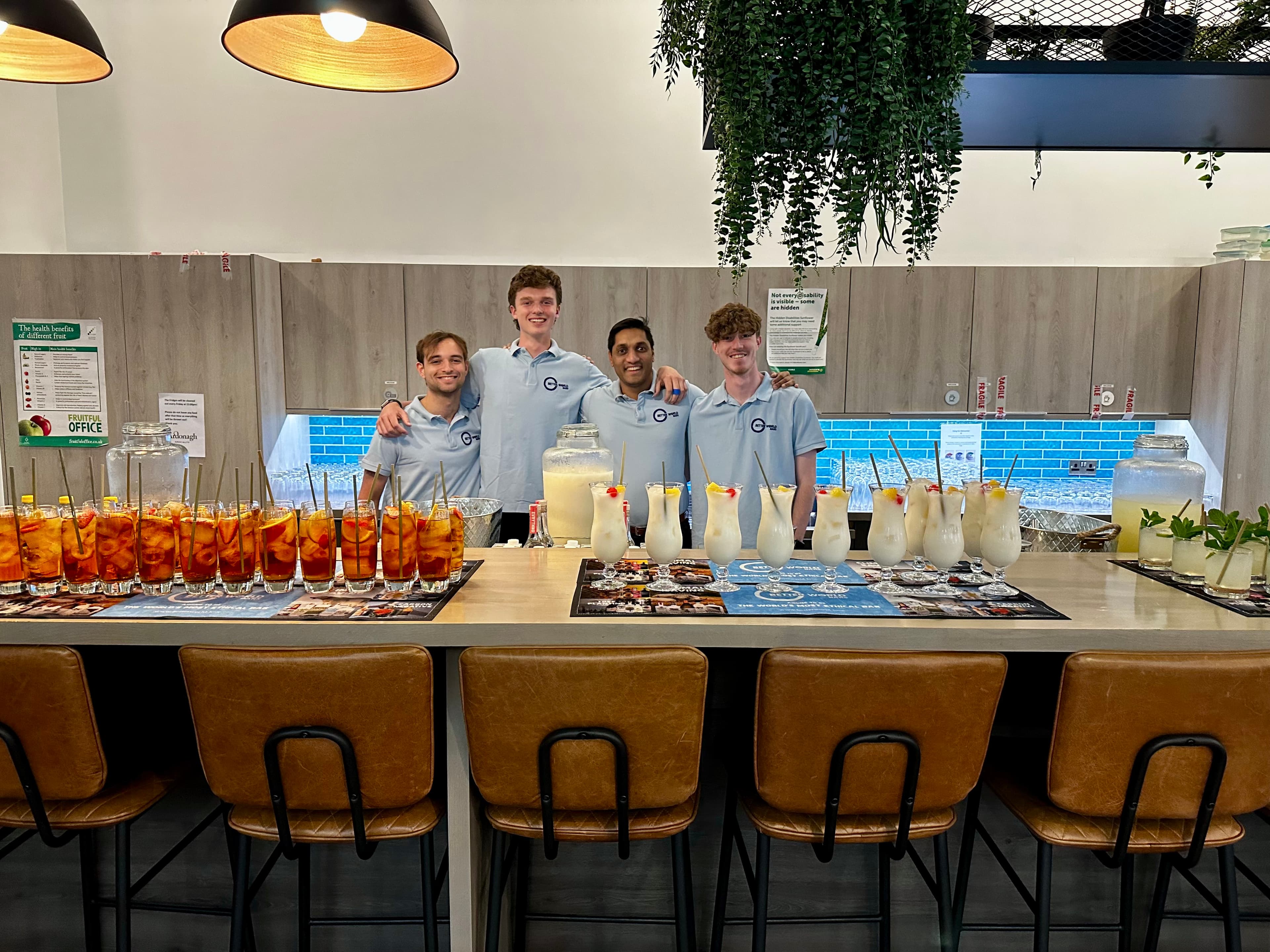 Four Better World Bar Hire team members behind an office bar transformation, the counter lined with freshly made cocktails ready to serve