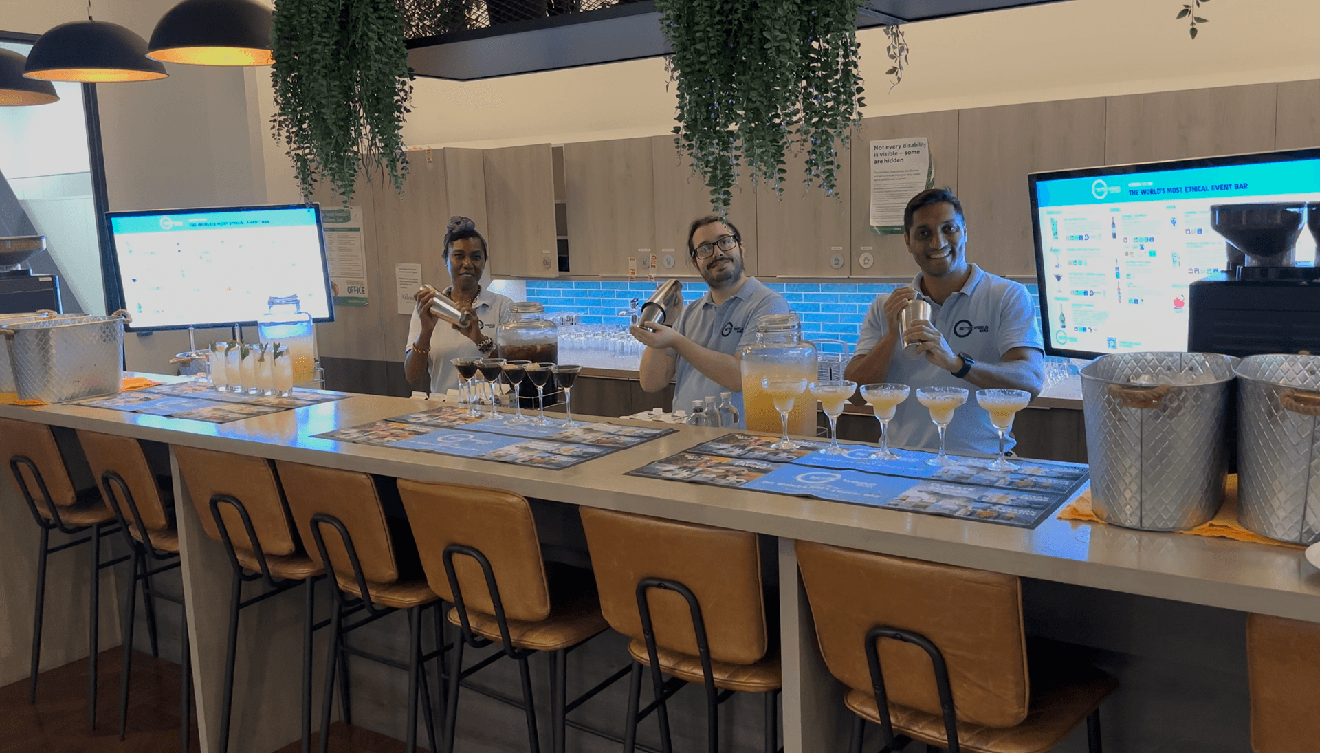 Three smiling expert bartenders holding cocktail shakers behind a premium event bar ready to discuss your vision and secure your date for your next sustainable celebration