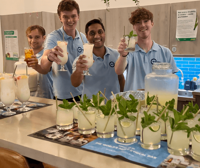 The BetterWorld team raising cocktails behind a bar lined with fresh mojitos