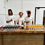 Three smiling team members standing behind a rustic wooden mobile bar covered in glasses of red and white wine