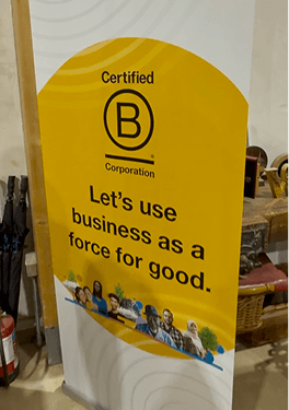 A pull up branding banner displaying the Certified B Corporation logo and the text let us use business as a force for good at the Kent community celebration