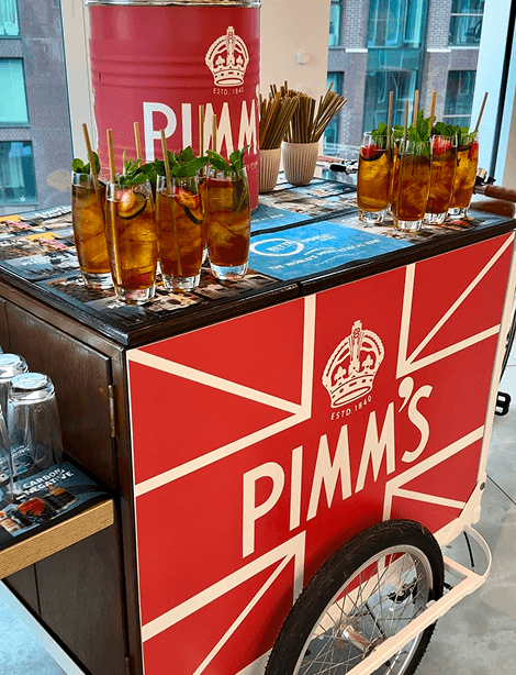 A branded Pimms tricycle featuring a large red Pimms keg and multiple fresh cocktails garnished with fresh fruit and mint ready for a corporate summer party