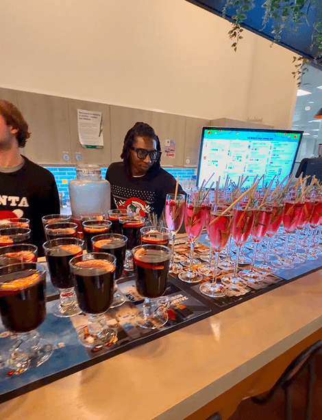 Cups of mulled wine and rosemary garnished festive cocktails lined along the office pop-up bar with the digital drinks menu behind