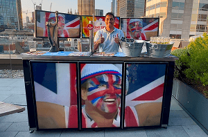 A professional bartender giving a thumbs up behind a digital pop up bar displaying custom video panels for a VIP event on a city rooftop