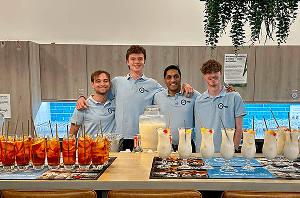 Four professional bartenders smiling behind an office kitchen counter transformed into a pop up cocktail bar for a corporate staff party