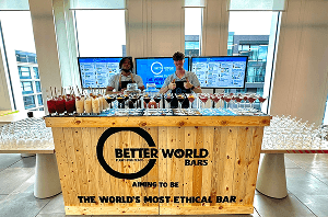 Two professional team members giving a thumbs up behind a rustic wooden pop up bar covered in freshly made sustainable cocktails.