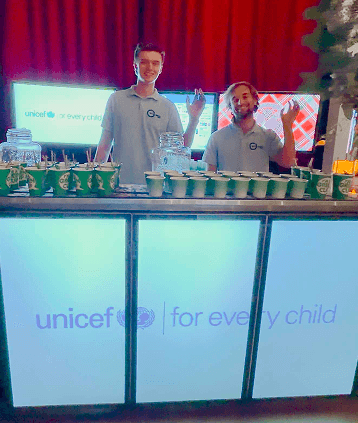 Two BetterWorld bartenders serving drinks from the digital mobile bar, its screens showing the UNICEF 'for every child' campaign