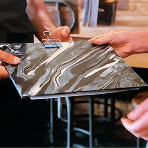 Two people holding a marble patterned clipboard made from recycled plastic packaging representing our circular economy innovation at the worlds most ethical pub READY TO MAKE A MEASURABLE DIFFERENCE?