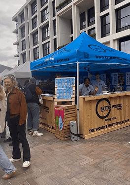 A wide view of the Better World Bars wooden pop up event bar with a blue canopy at a busy outdoor festival