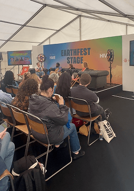 A wide view of a seated audience watching a live panel discussion on the main stage at a sustainability festival