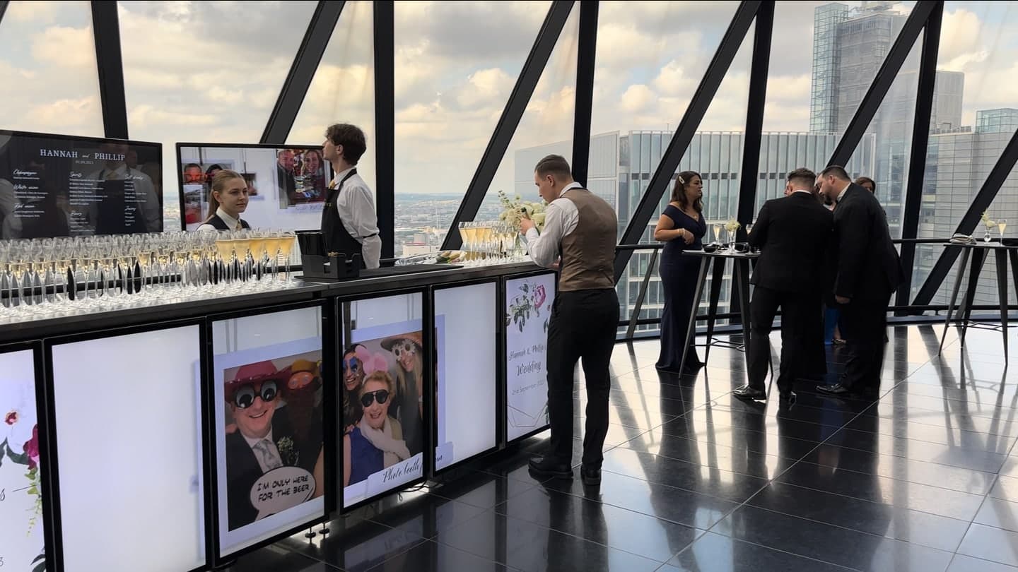 A bartender opening a bottle of champagne for wedding guests beside the digital event bar inside the Gherkin building