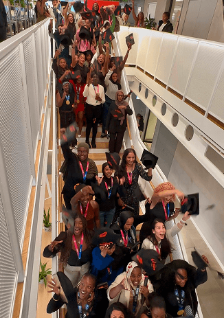 A large group of women celebrating on a modern staircase throwing their graduation caps into the air at a corporate event